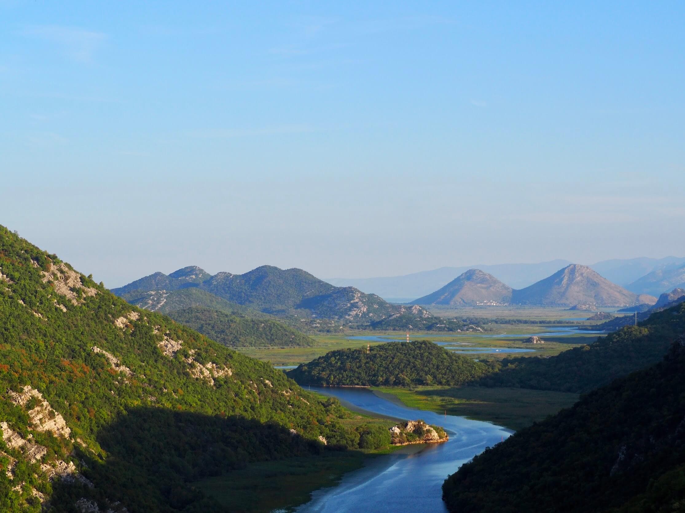 Ladera boscosa reflejada en las aguas tranquilas del lago Skadar, Montenegro